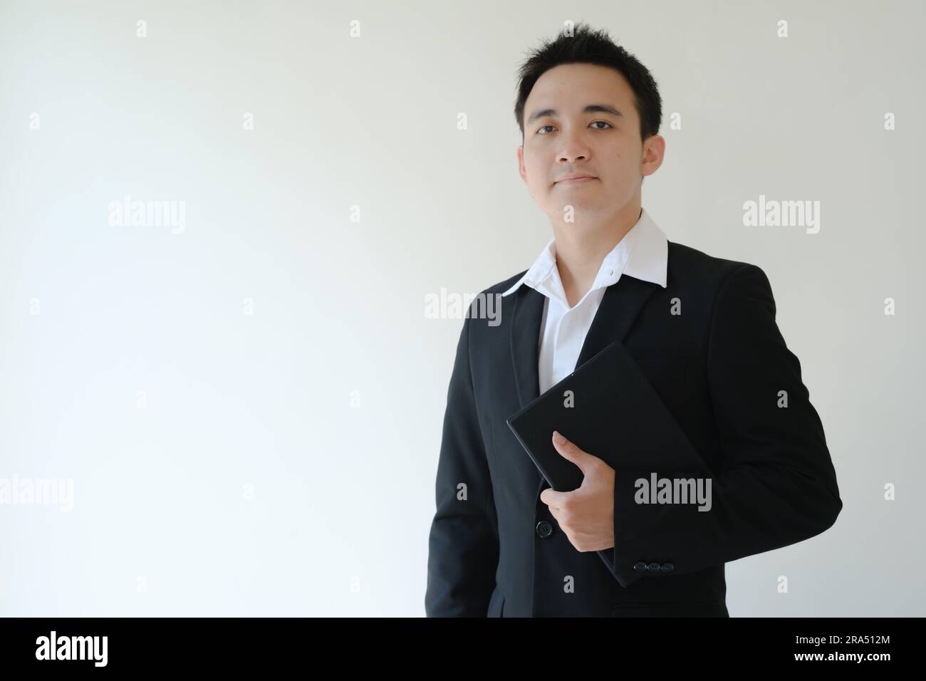 Ein junger asiatischer Geschäftsmann, der ein Tablet in der Hand hält und in die Kamera schaut. Isolierter weißer Hintergrund. Stockfoto