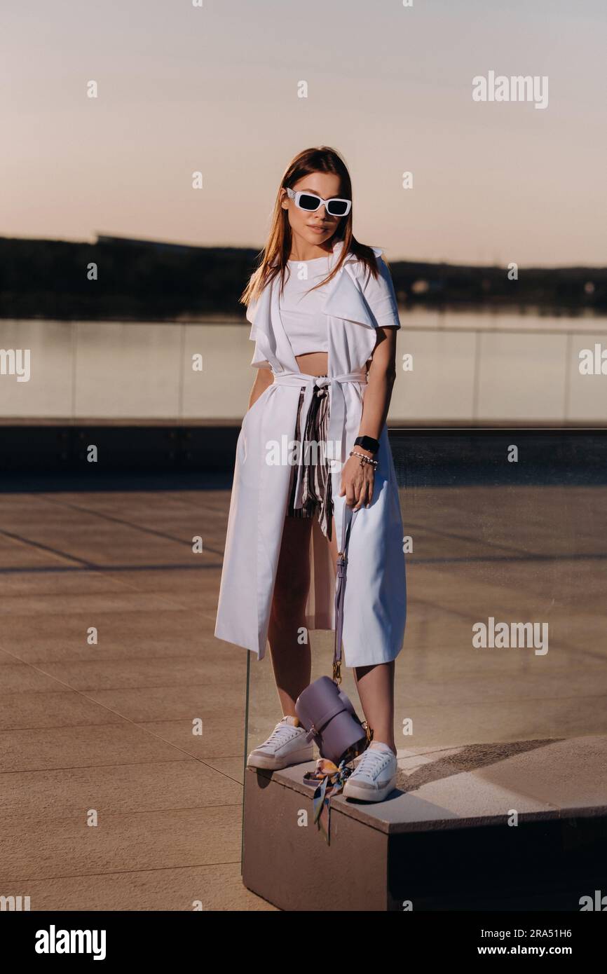 Ein stilvolles Mädchen mit Brille und einem weißen Sommerkittel in der Stadt mit einer Handtasche. Stockfoto