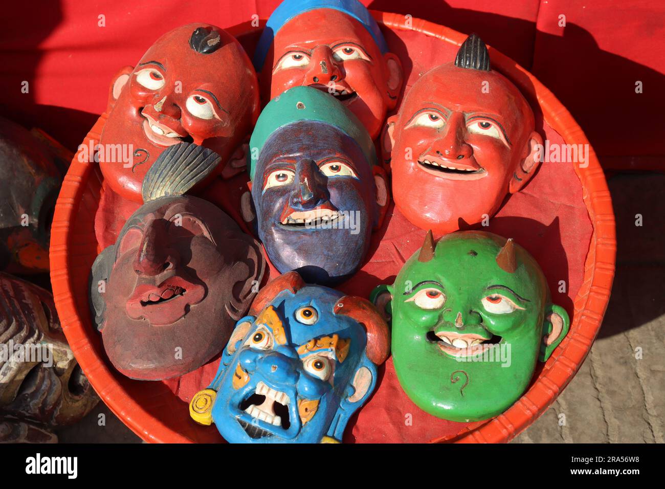 Holzmaske mit lustigen Gesichtern und wütendem Gesicht in einem Korb auf dem Markt von Nepal zum Verkauf gehalten. Farbenfrohe Holzmasken-Sammlung Stockfoto