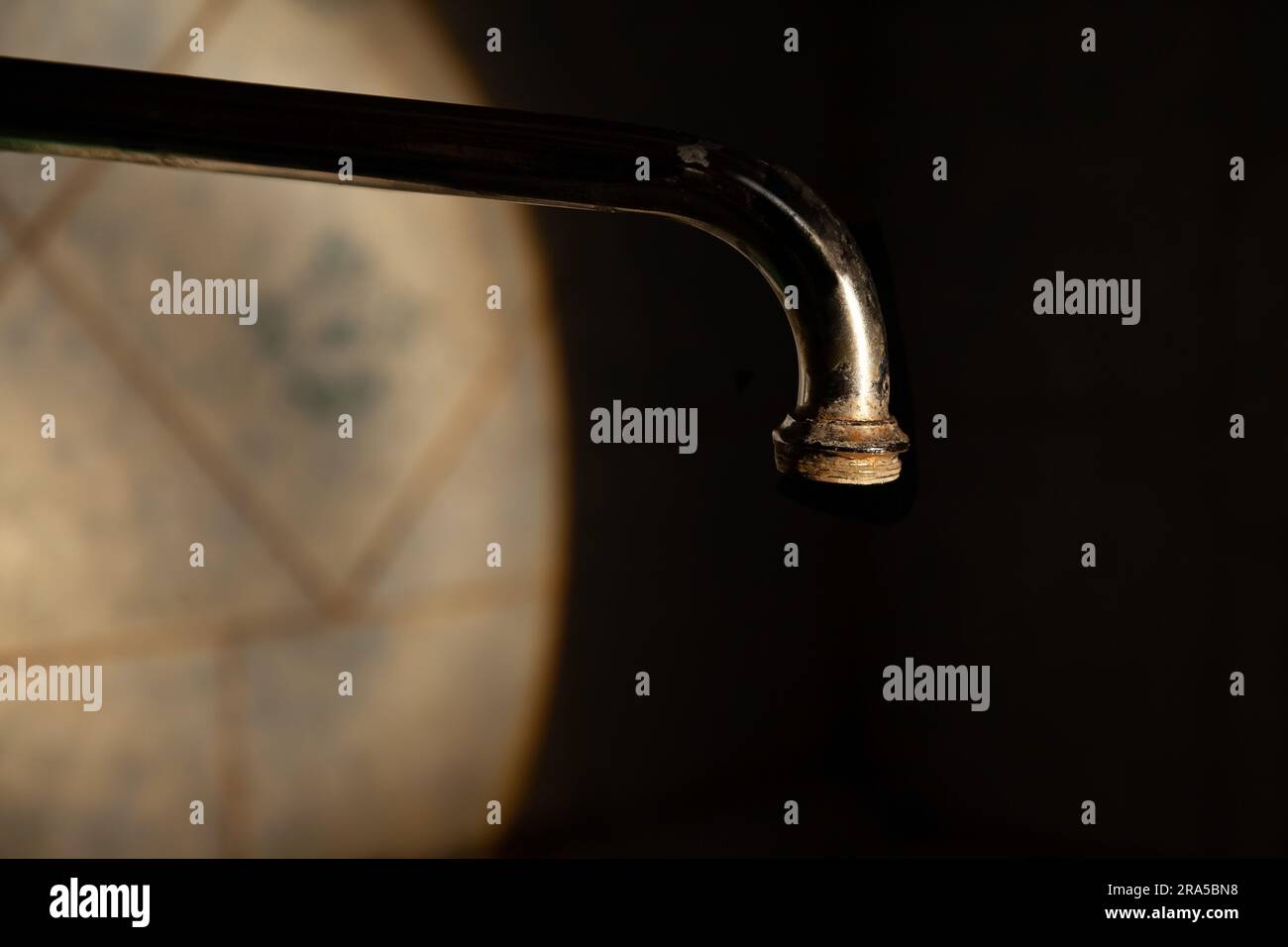 Alter Wasserhahn im Dunkeln auf schwarzem Hintergrund, in einem Lichtfleck Stockfoto