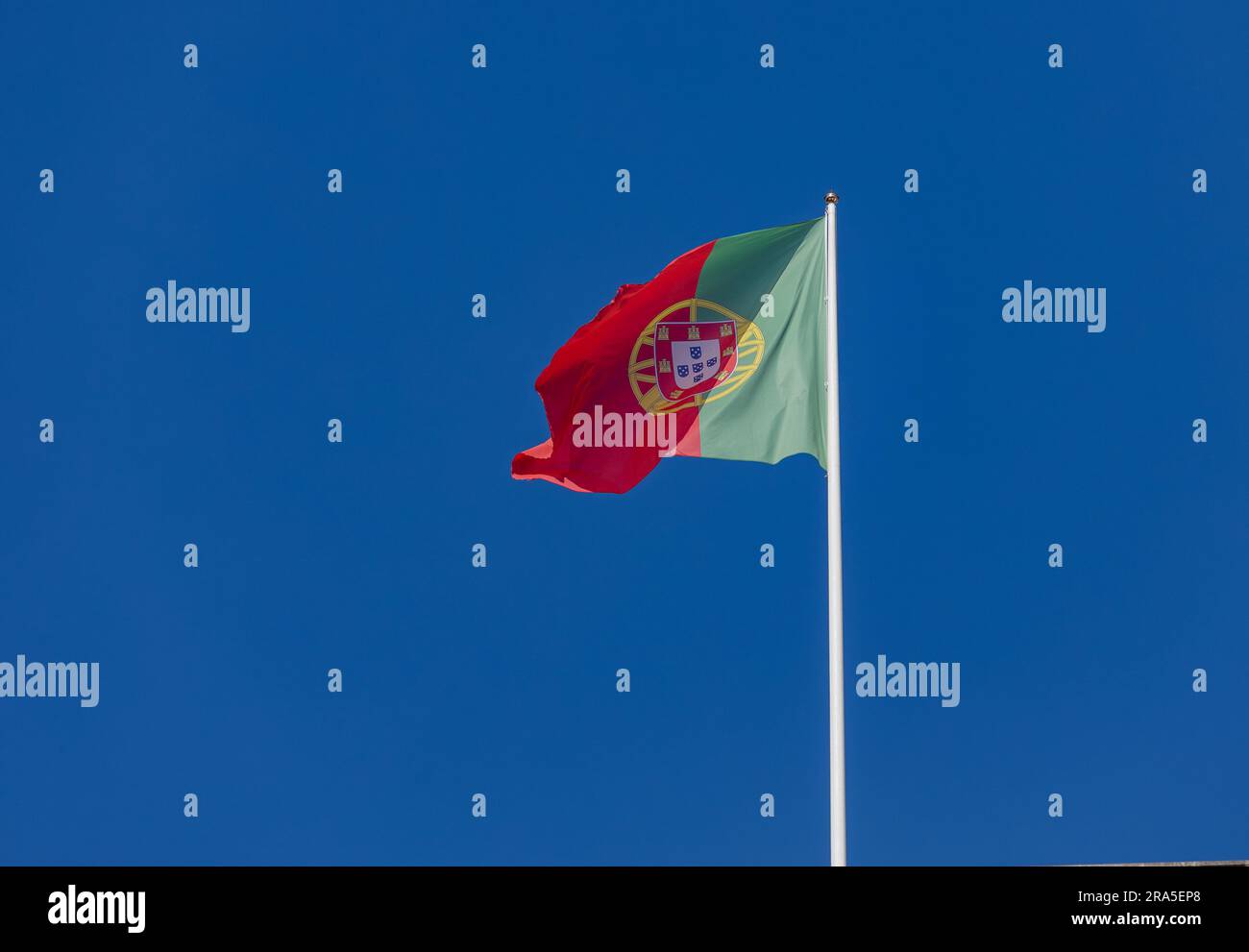 portugiesische Flagge am Stab, winkend im wolkenlosen blauen Himmelshintergrund Stockfoto