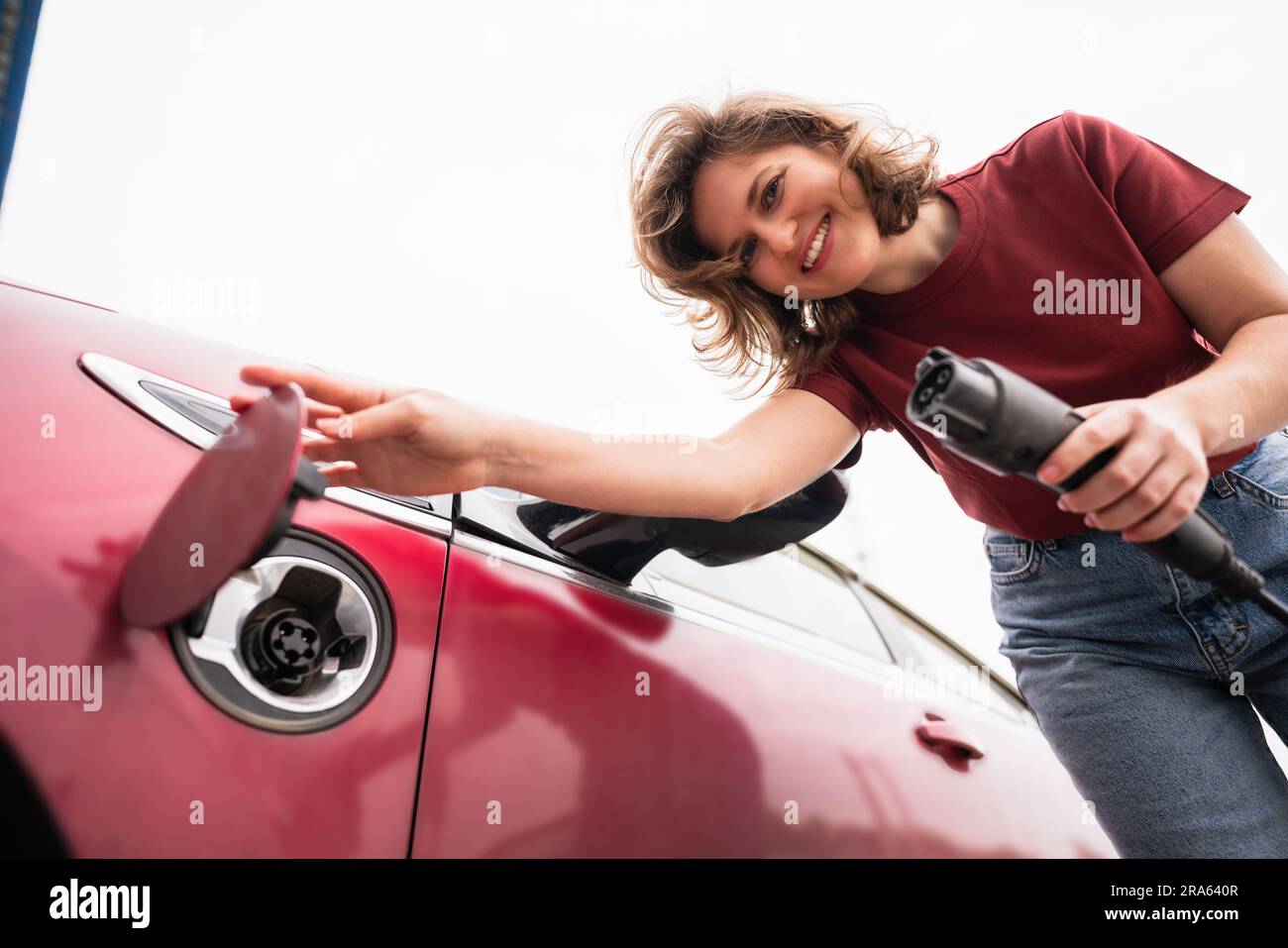 Frau mit Smartphone, die ein rotes Elektroauto auflädt Stockfoto