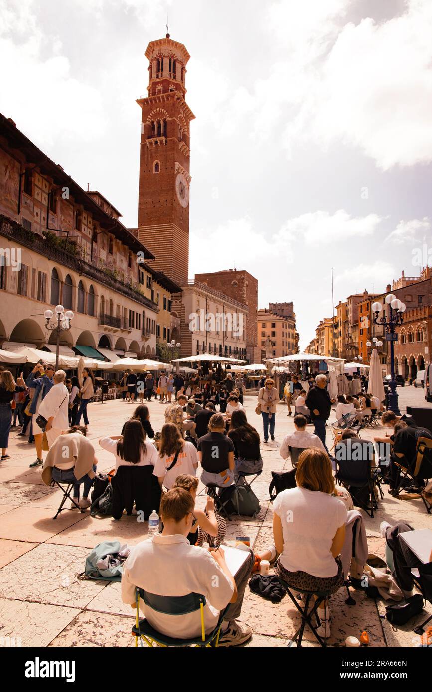 Menschen, die auf der Piazza delle Erbe oder dem Marktplatz, Verona, Veneto Italien Europa sitzen, im Frühlingssonnenschein im Mai. Reisen und Lifestyle in Italien Stockfoto