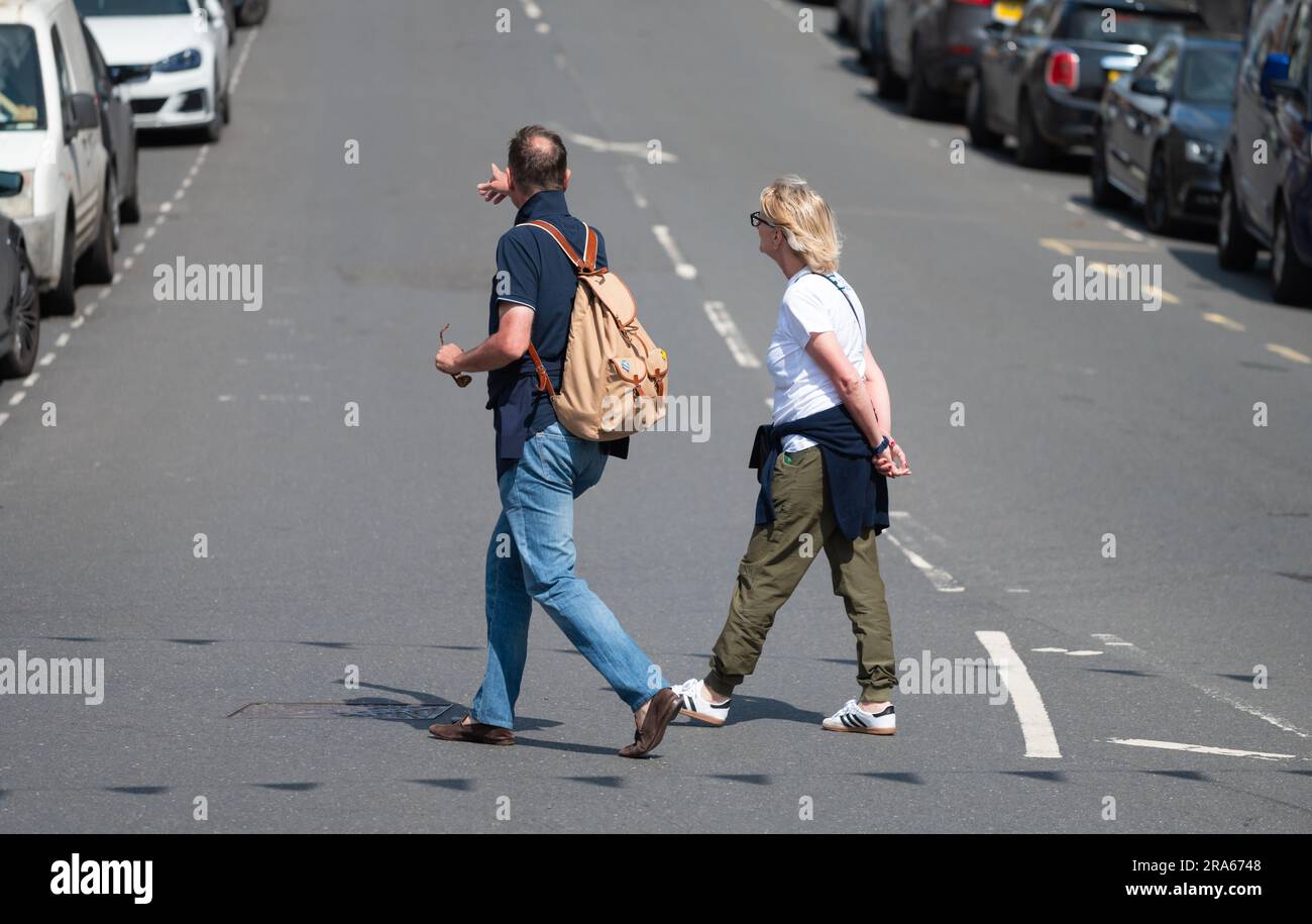 Ein paar Leute, wahrscheinlich Touristen, laufen über eine Straße in einer britischen Stadt in England. Leute, die die Straße überqueren. Stockfoto