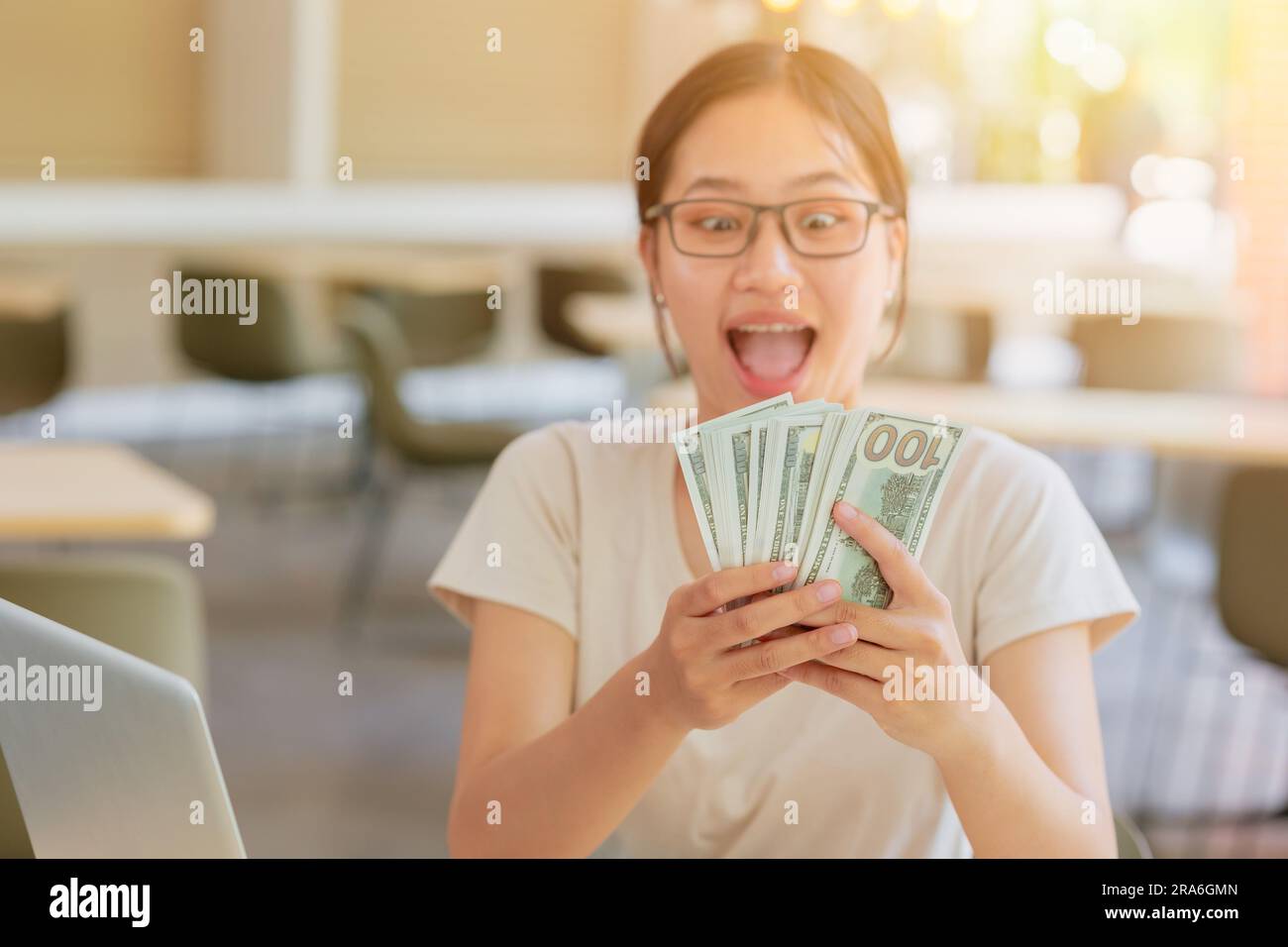 Junge Studentin an der Universität, die gerne viel Bargeld für Teilzeitarbeit im Internet verdient. Stockfoto