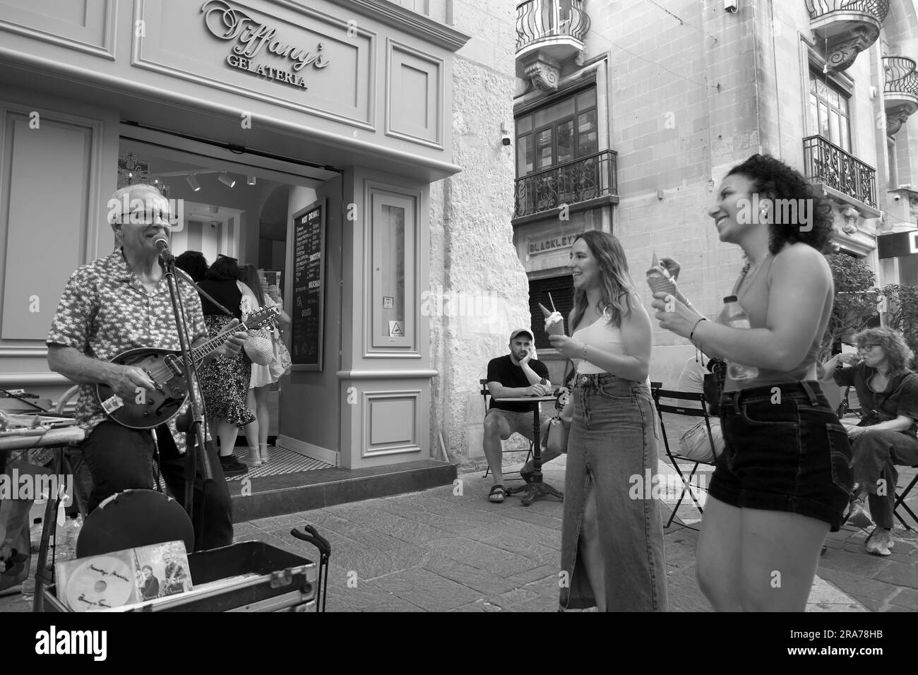 Schwarz-Weiß zwei junge Touristen singen gern einen Straßenkünstler in der Republic Street, Valletta, Malta Stockfoto