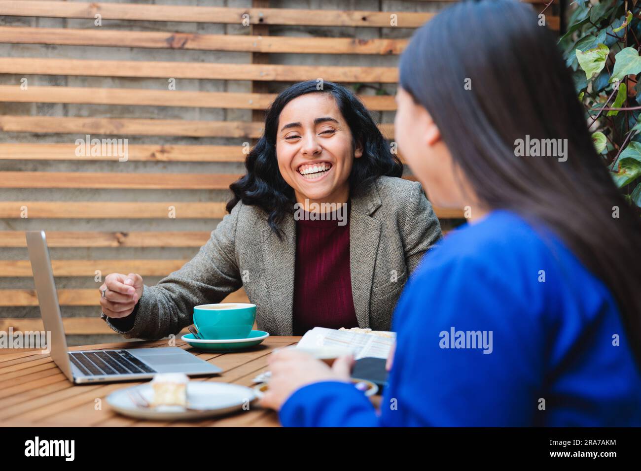 Finanzsicherheits-Gespräch: Junge Latina, die eine Lebensversicherung an eine andere Frau in einem gemütlichen Café verkauft Stockfoto
