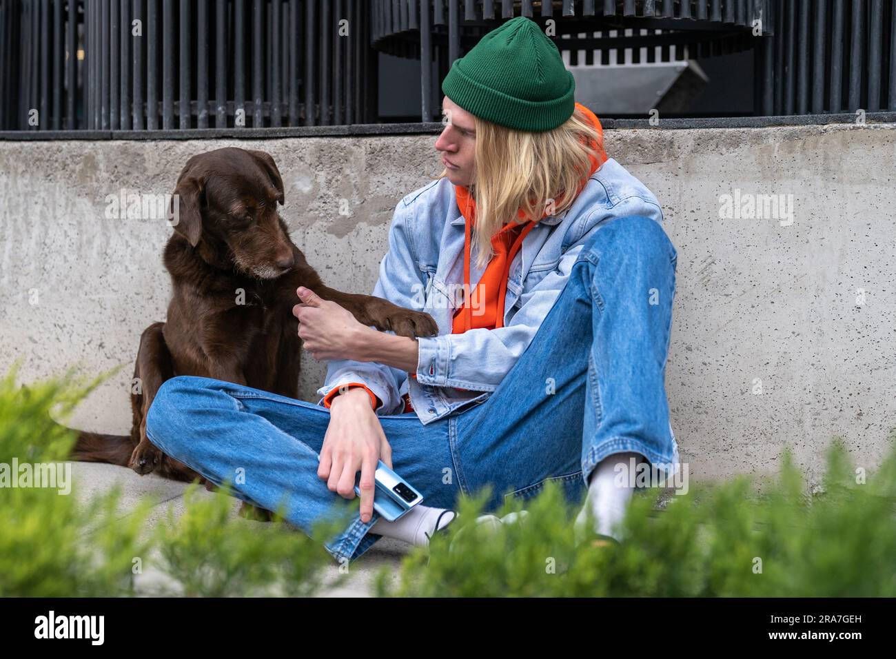 Ein Hipster-Millennials-Typ und ein süßer, obdachloser Hund, der draußen zusammen sitzt Stockfoto