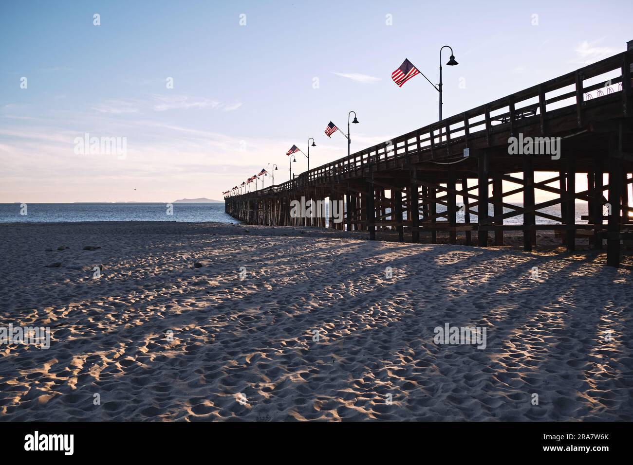 Der Ventura Pier biegt sich in die Ferne und ist an Thanksgiving mit US-Flaggen geschmückt. Die späte Sonne erzeugt am Sandstrand eindrucksvolle Schatten. Stockfoto