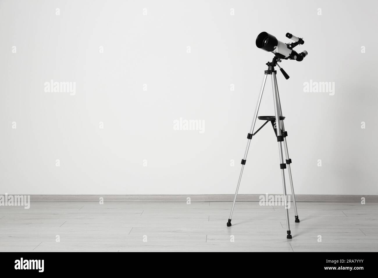 Stativ mit modernem Teleskop nahe der weißen Wand. Platz für Text Stockfoto