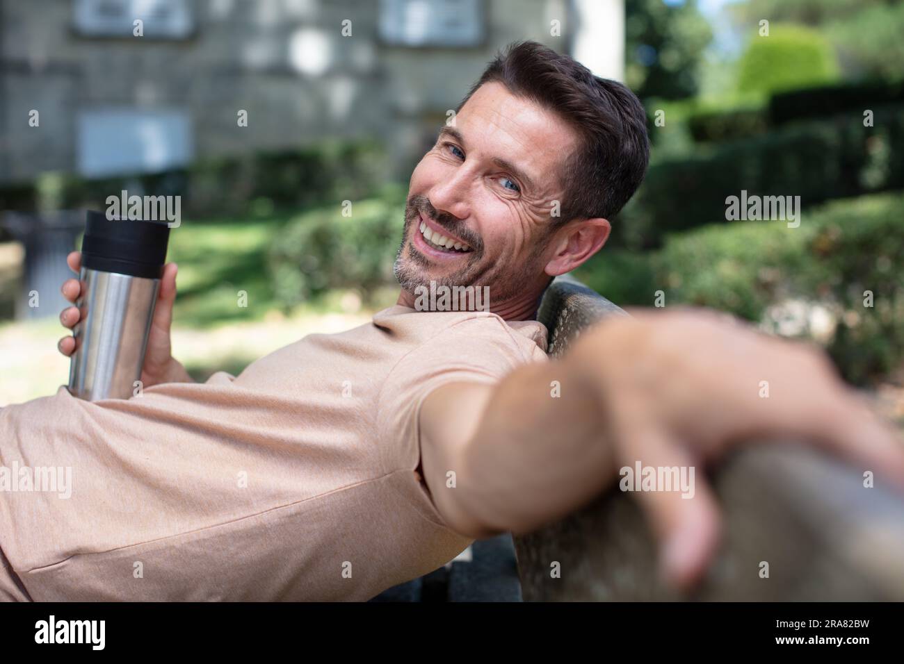 Ein Mann, der sich auf einer Bank mit einem isolierten Becher entspannt Stockfoto