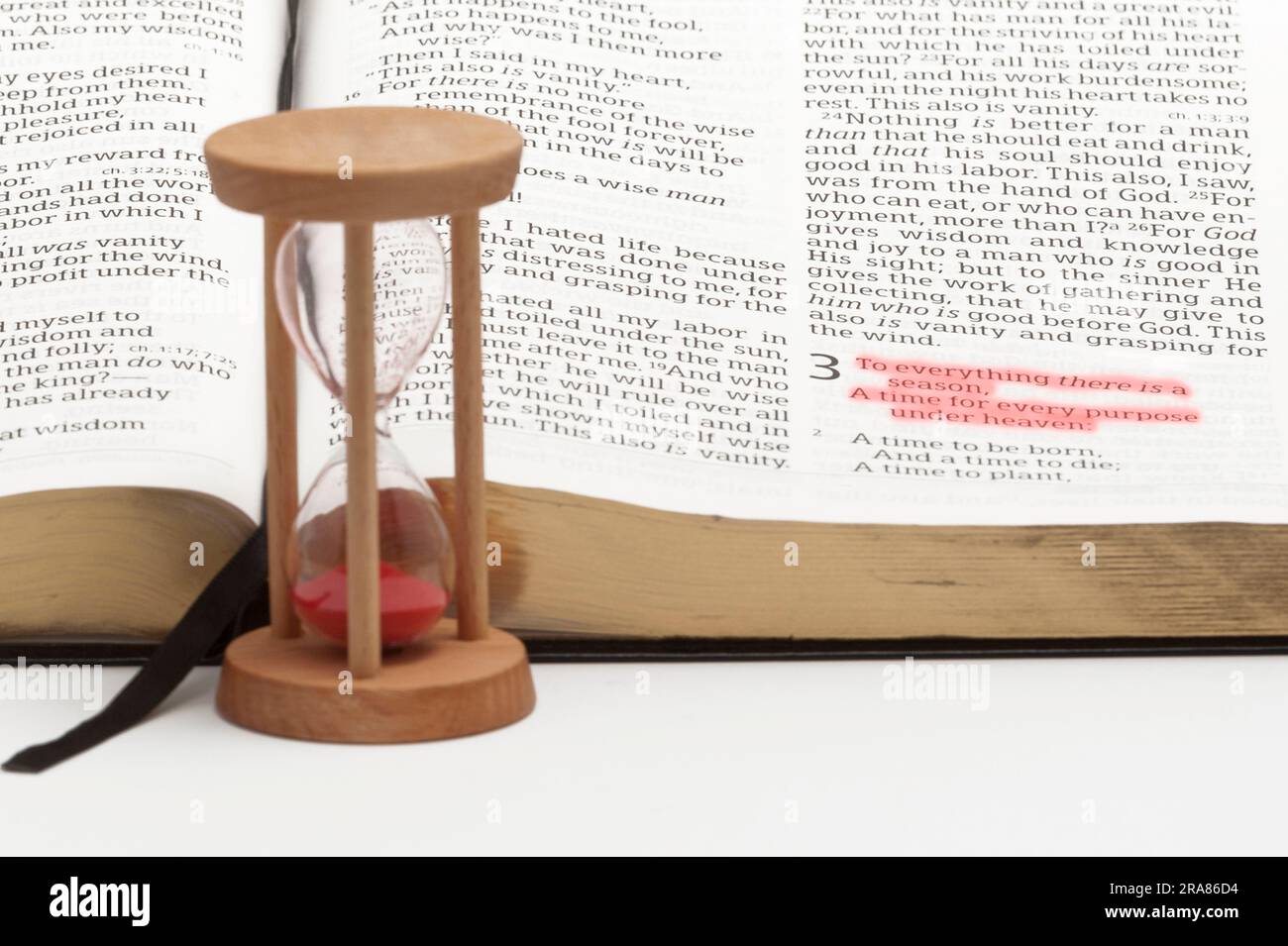 Sanduhr und offene bibel über das Buch des Kirchenlehrers mit selektivem Fokus auf Vers 1 von Kapitel 3, rot hervorgehoben. Isoliert auf weißem Hintergrund. Stockfoto