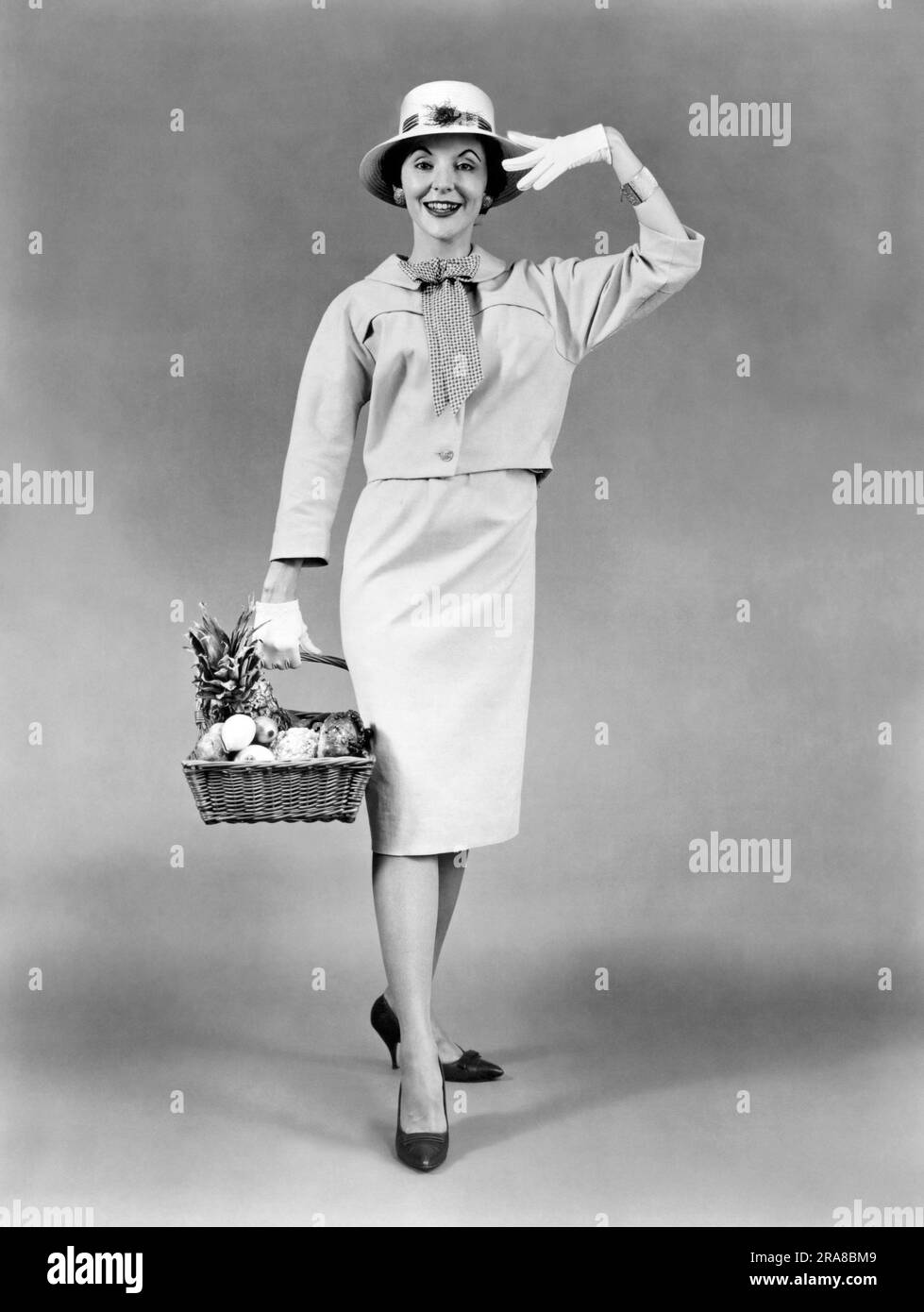 Vereinigte Staaten: 1959. Eine Frau mit einem Korb voller Produkte trägt als Sommerkleidung ein Kostüm aus Baumwollbeuteln mit McCalls Muster 5082 und 5336. Stockfoto