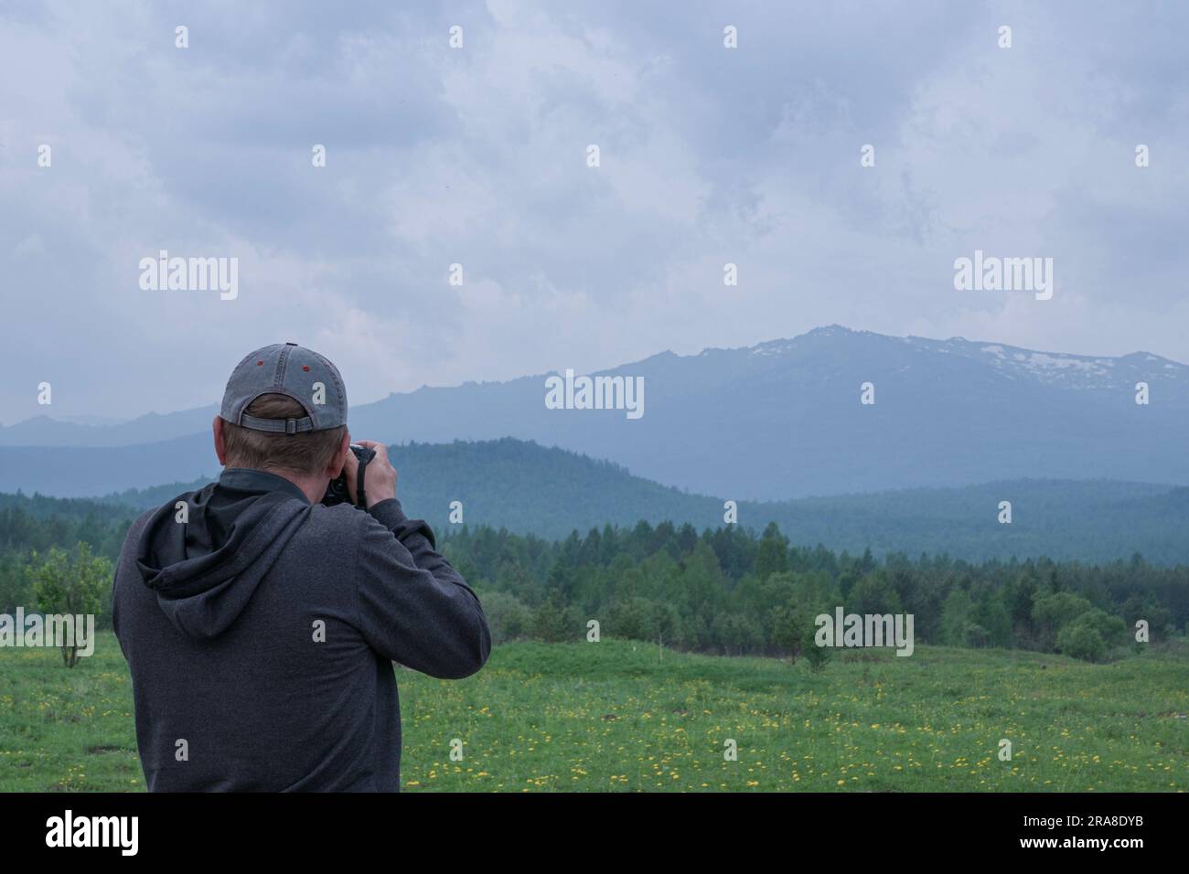 Der Fotograf fotografiert die Landschaft - Berge und Hügel, Nadelwälder und Lichtergärten im Vordergrund. Blick von hinten. Es gibt einen CO Stockfoto