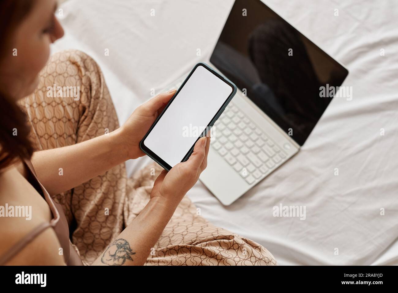 Minimale Draufsicht auf junge Frau mit Laptop und Smartphone, leerer weißer Bildschirm auf dem Bett, Kopierbereich Stockfoto