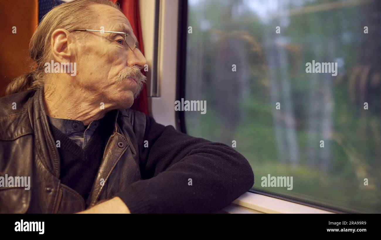 Die Nahaufnahme eines älteren Mannes mit Brille reist in einem Zug und schaut aus dem Fenster Stockfoto
