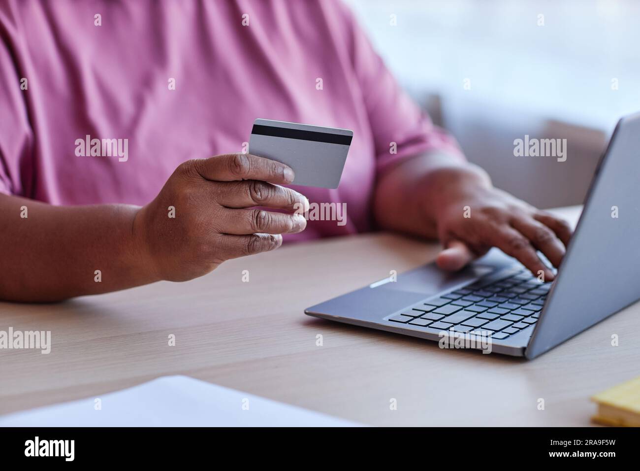 Konzentrieren Sie sich auf die Hand einer älteren Frau mit Kreditkarte, die am Schreibtisch sitzt und ein Notebook verwendet, während sie im Online-Shop Dinge bestellt und bezahlt Stockfoto