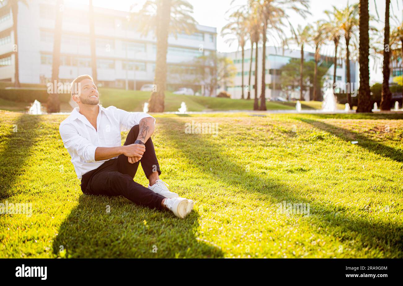 Work-Life-Balance-Konzept. Glücklicher junger europäischer Geschäftsmann, der auf dem Rasen im Park sitzt, Pause macht und sich ausruht, freier Platz Stockfoto