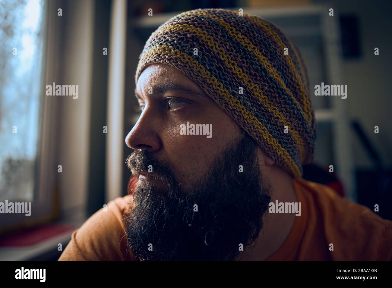 Ein Mann mit einem Bart, der einen gestreiften Hut und ein T-Shirt trägt und zum Fenster hinaufblickt Stockfoto