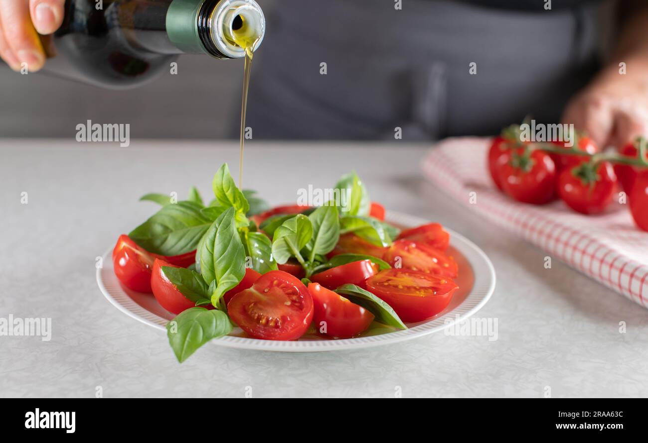 Ich gieße Olivenöl in eine Flasche über einen Kirschtomatensalat mit Basilikumblatt Stockfoto