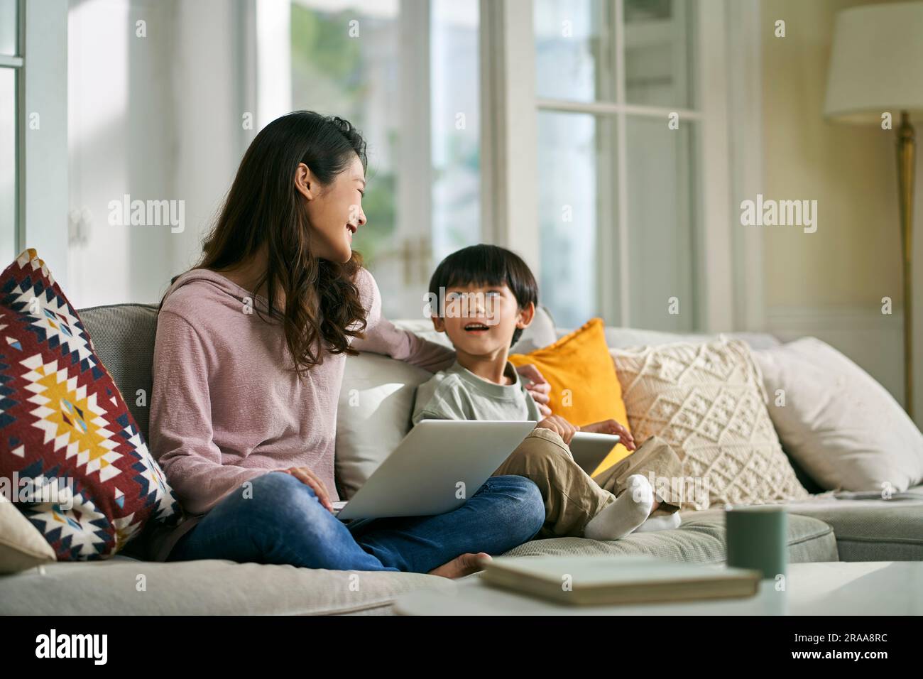 Junge asiatische Mutter und fünfjähriger Sohn sitzen zu Hause auf der Couch und unterhalten sich angenehm Stockfoto