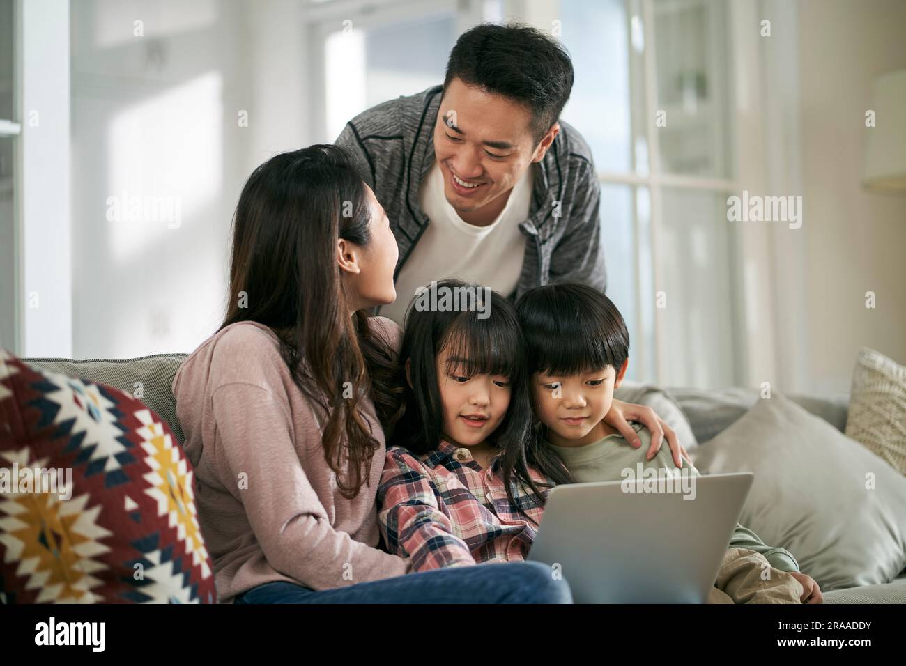 Glückliches junges asiatisches Paar mit zwei Kindern, das zu Hause auf dem Familientisch saß und zusammen einen Laptop benutzte Stockfoto