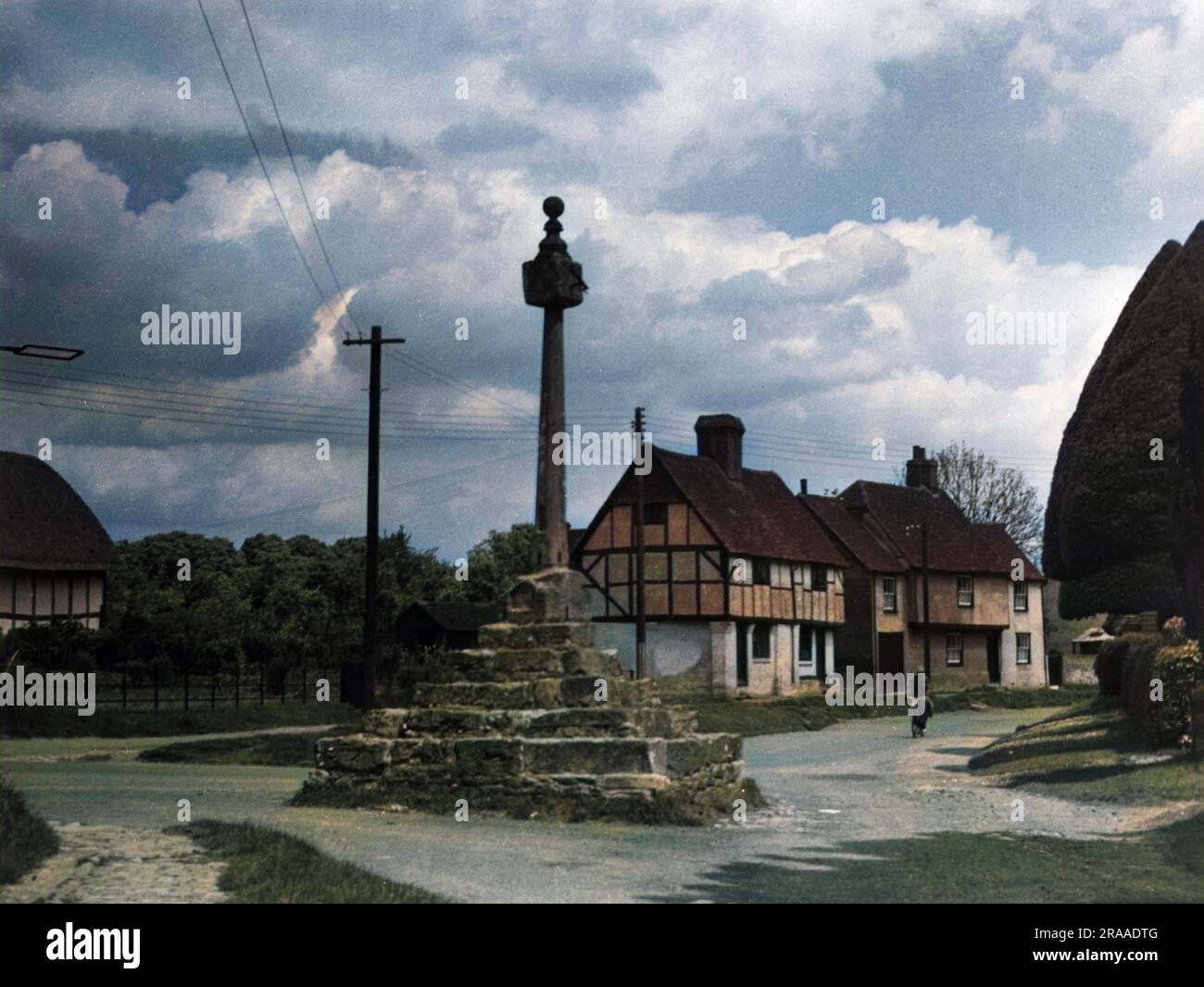 Fachwerkhäuser und das alte steinerne Dorfkreuz, das oben auf dem Schacht drei Sonnenkreuze hat, East Hagbourne, Berkshire, England. Datum: 1950er Stockfoto