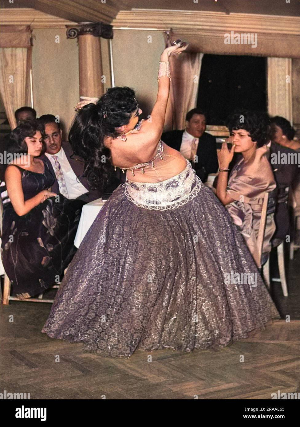 Zwei weibliche Gäste sind nicht erfreut, wenn eine enthusiastische Bauchtänzerin an ihrem Tisch im Khased Kheir Casino in Kairo, Ägypten tanzt. Datum: Anfang 1960er Stockfoto