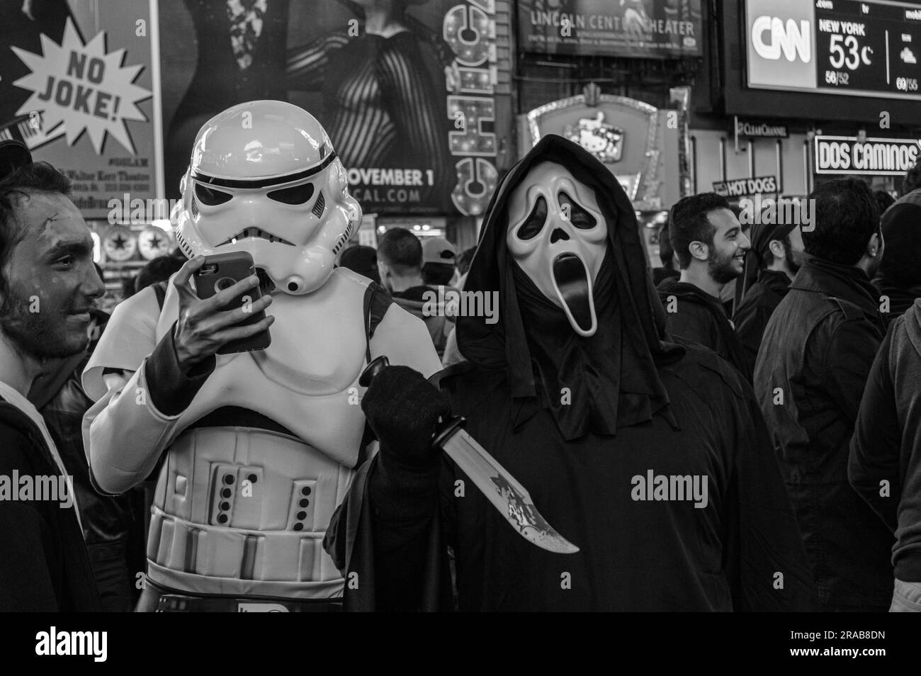Zwei Leute mit Masken, einer überprüft sein Handy, steht in Times Square. An Halloween. Stockfoto