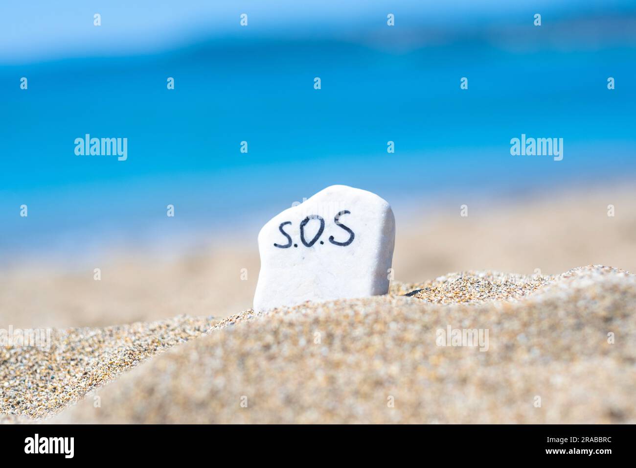 SOS - das Wort, das auf einem Stein im Sand am Strand vor dem Hintergrund des türkisfarbenen Meeres zeichnet. Hilfe! Hilfe! Rette den Ozean. Ökologie und Umwelt Stockfoto