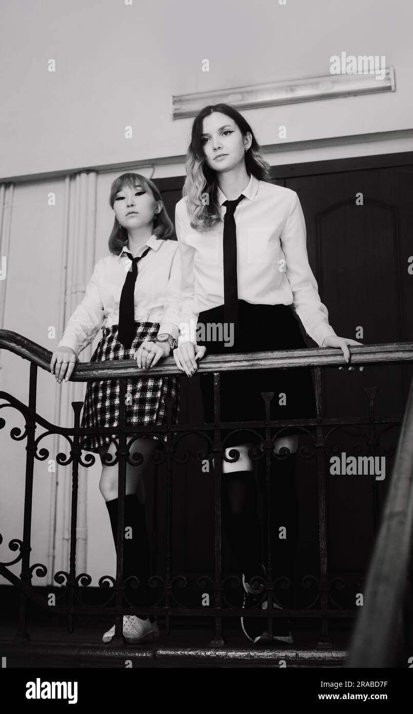 Das Schwarz-Weiß-Bild von zwei hübschen und seriös aussehenden Schulmädchen in weißen Hemden und schwarzen Krawatten steht auf einer Schultreppe Stockfoto