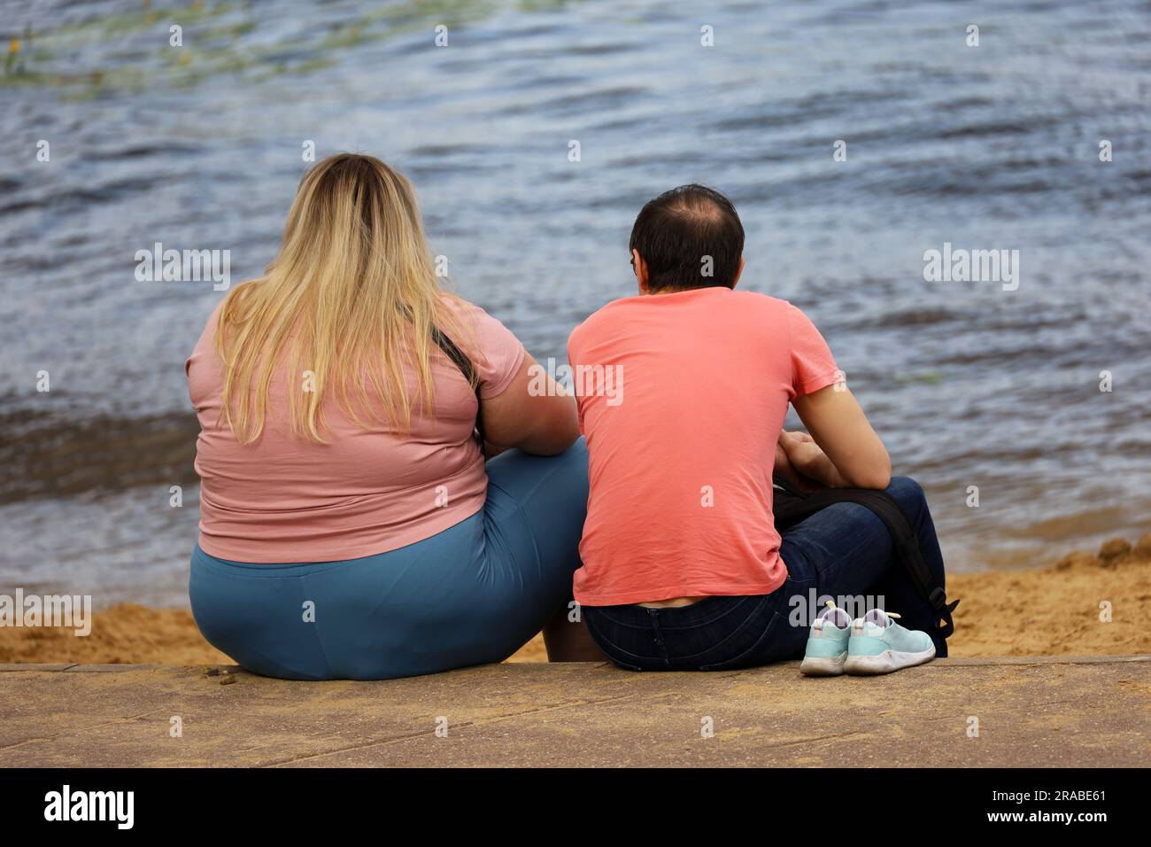 Ein Paar, das am Sommerstrand sitzt. Dicke Frau und schlanker Mann, Beziehung und Fürsorge Stockfoto