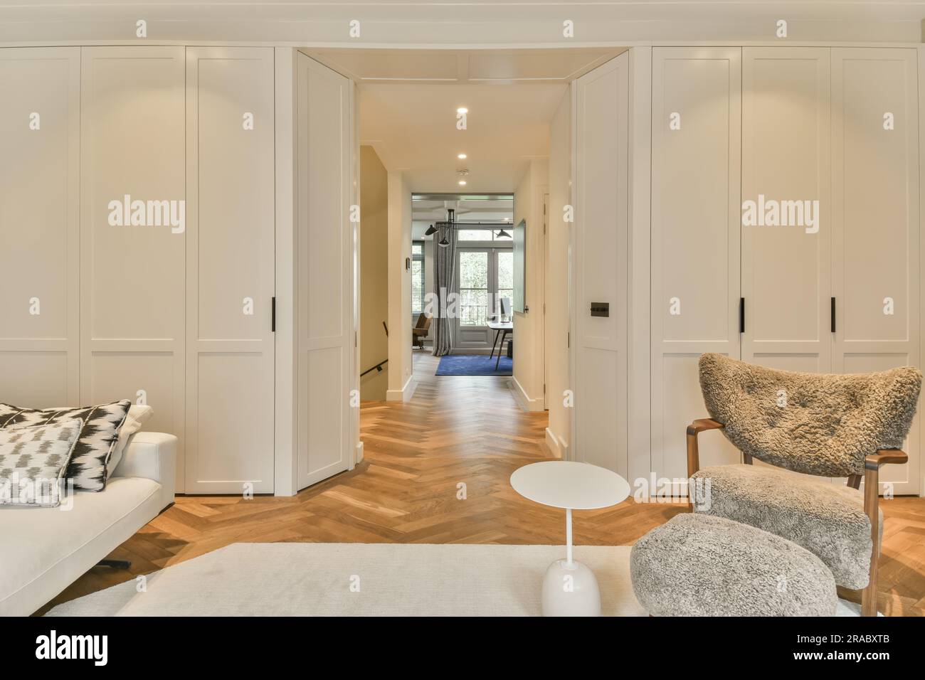 Ein Wohnzimmer mit weißen Wänden und Hartholzfußboden. Das Zimmer ist in neutralen Farbtönen eingerichtet, einschließlich Holzfußboden Stockfoto