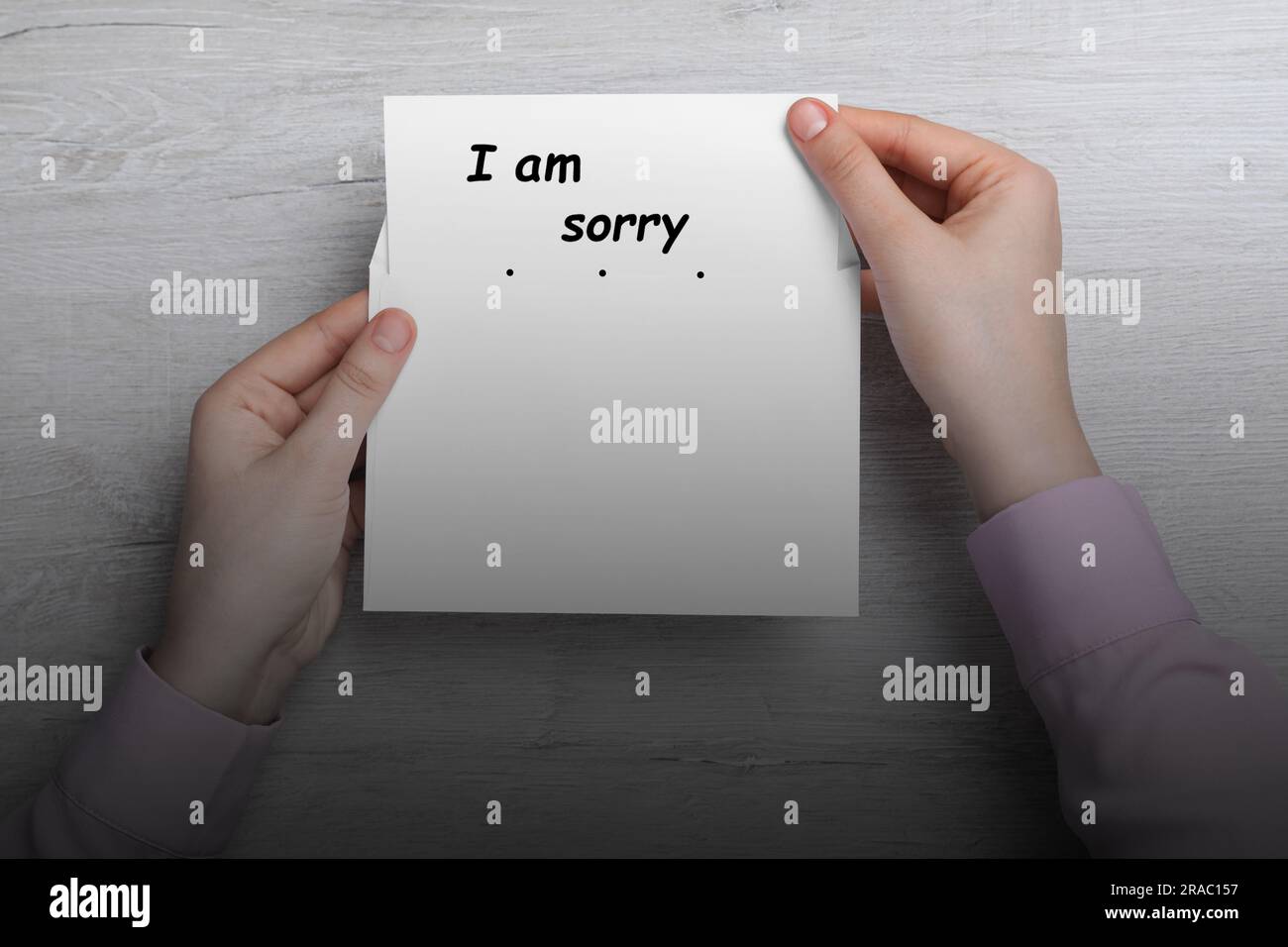 Entschuldigung. Eine Frau, die die Karte mit dem Spruch "Es tut mir leid" aus dem Umschlag am Holztisch nimmt, Draufsicht Stockfoto