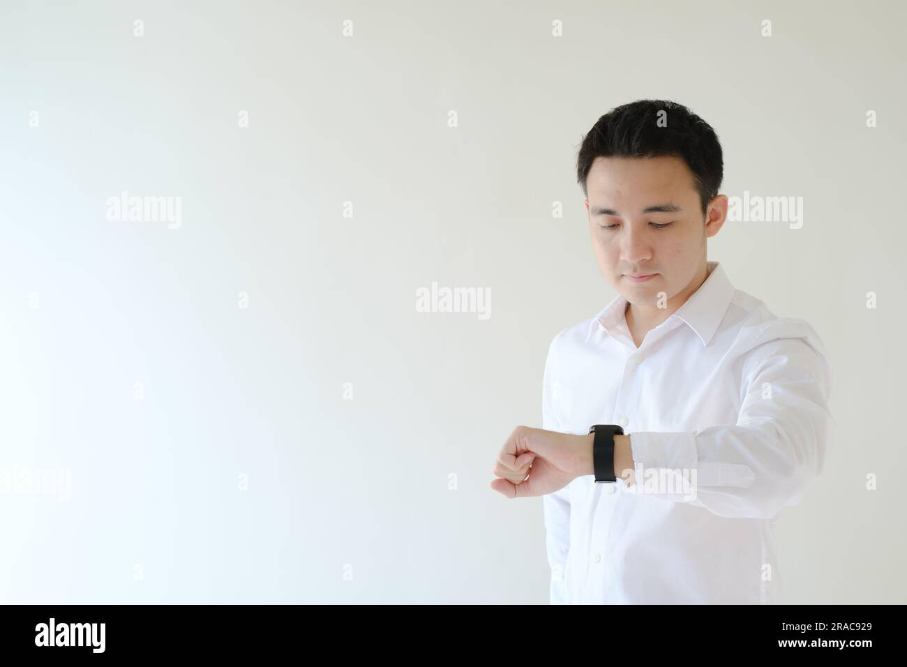 Ein junger asiatischer Mann mit weißem Hemd schaut auf seine Uhr. Isolierter weißer Hintergrund. Stockfoto