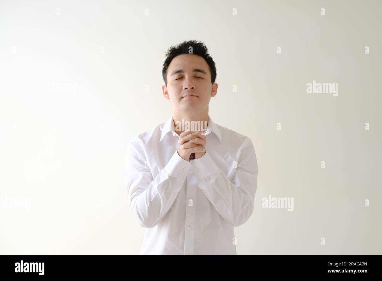 Ein junger Asiate, der ein weißes Hemd trägt und betet. Isolierter weißer Hintergrund. Stockfoto
