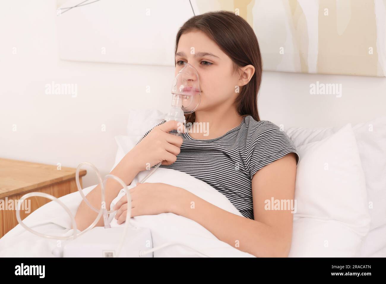 Süßes Mädchen, das zu Hause einen Vernebler zur Inhalation am Bett benutzt Stockfoto