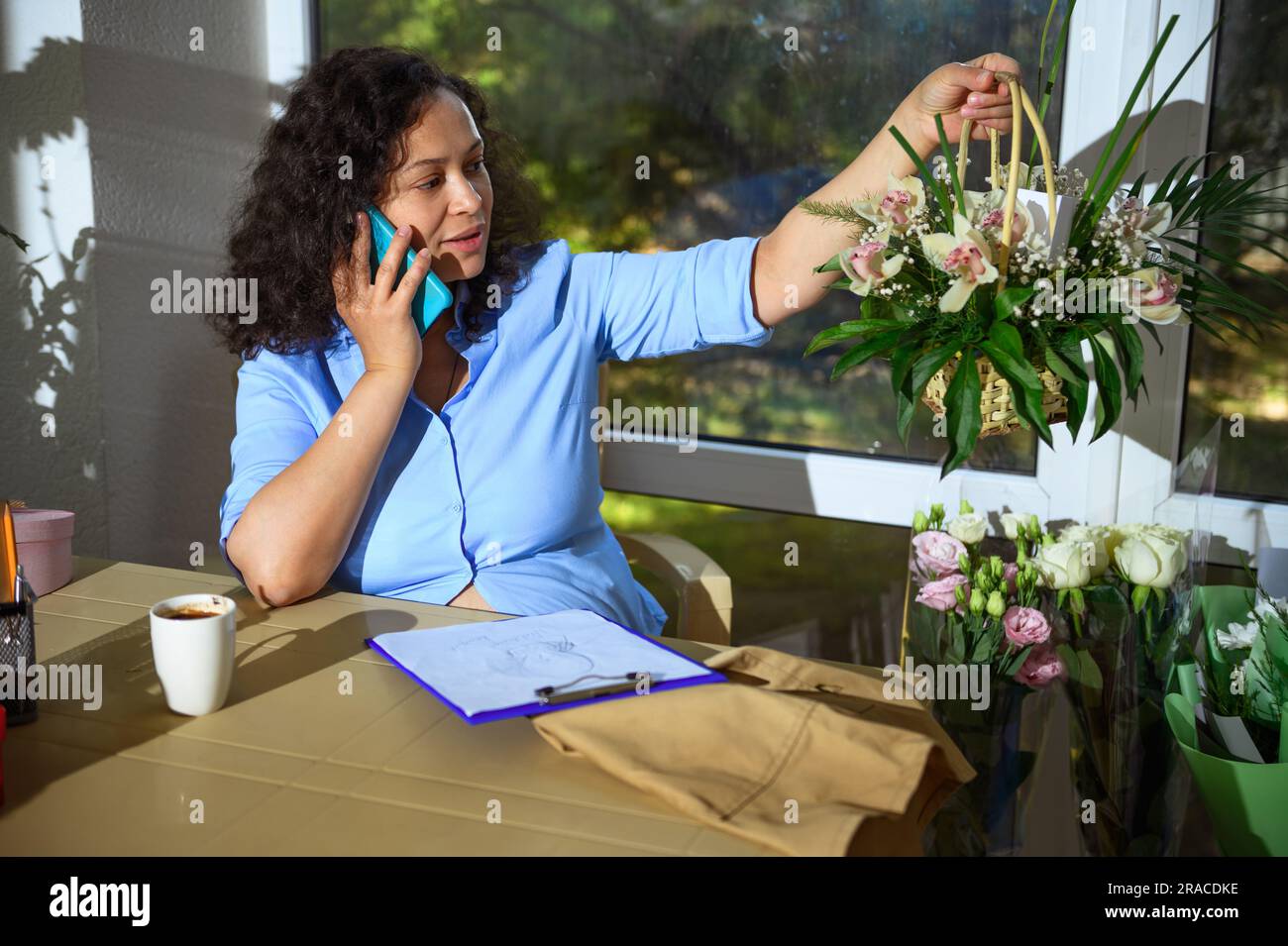 Selbstbewusste Blumenunternehmerin, die mit dem Handy spricht, einen Korb mit Blumen hält, über Bestellungen für besondere Festtage spricht Stockfoto