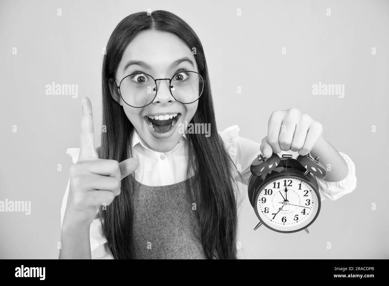 Porträt eines Teenagers mit Uhr Alrm, Zeit und Deadline. Studioaufnahme isoliert auf gelbem Hintergrund. Überrascht Teenager Mädchen. Stockfoto