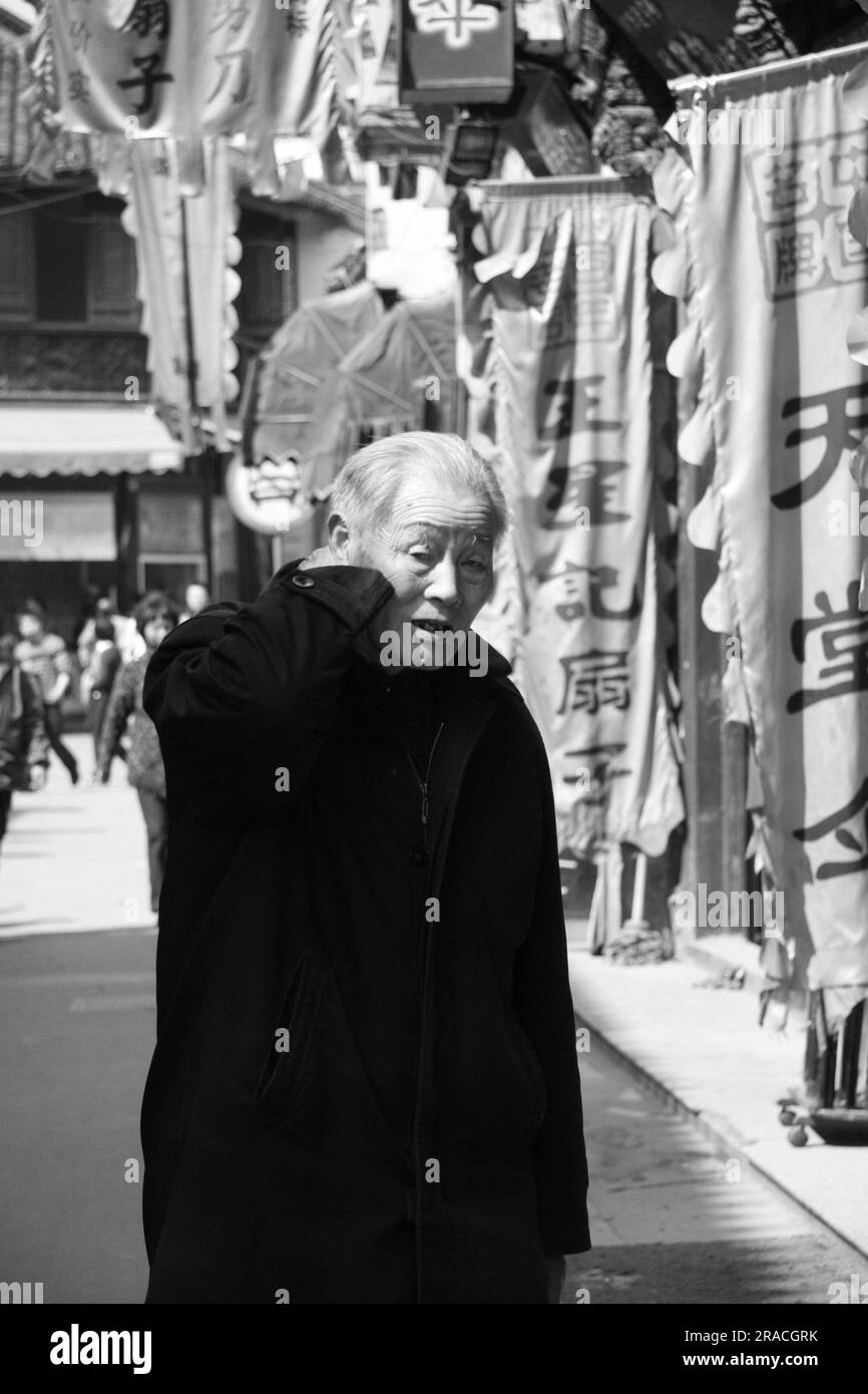 Ein älterer Mann in Black, der an Geschäften in der Hefeng Jie Fußgängerzone in Hangzhou China vorbeigeht Stockfoto