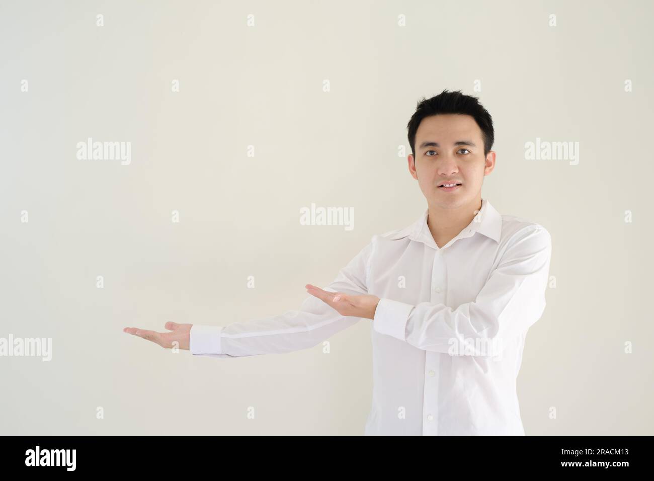 Ein junger asiatischer Mann, der ein weißes Hemd trägt, öffnet seine rechte Hand zur rechten Seite und sieht sie an. Isolierter weißer Hintergrund. Stockfoto Ein junger asiatischer Mann, der ein weißes Hemd trägt, öffnet seine rechte Hand zur rechten Seite und sieht sie an. Isolierter weißer Hintergrund. Stockfoto