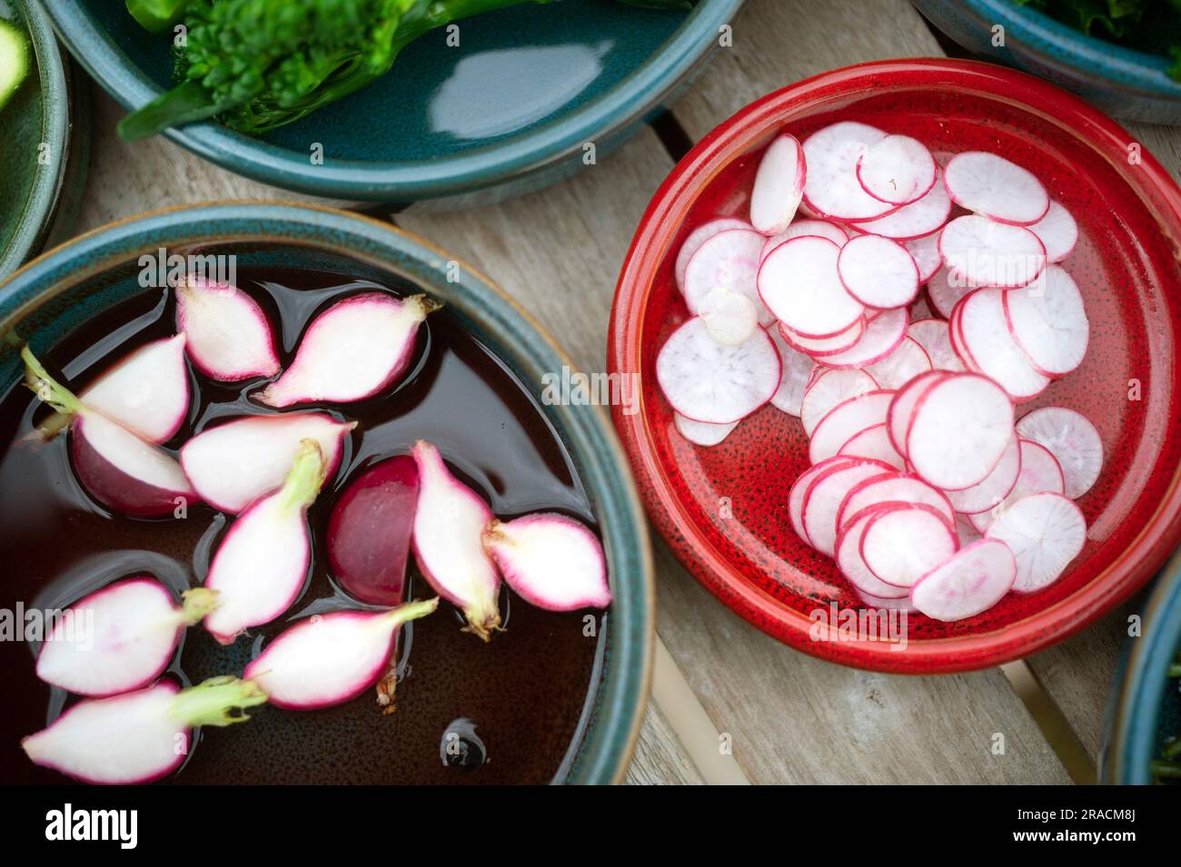 Radieschen in Scheiben, die in grünen und roten Keramikschüsseln eingespritzt werden Stockfoto