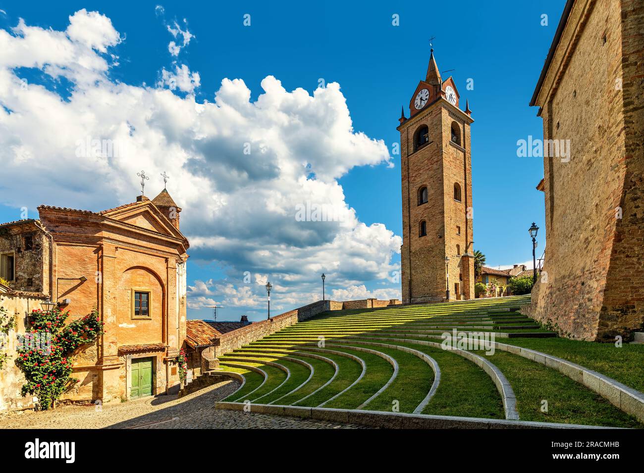 Kleine Kirche, Glockenturm und Open-Air-Amphitheater unter blauem Himmel mit weißen Wolken in der Kleinstadt Monforte d'Alba, Italien. Stockfoto