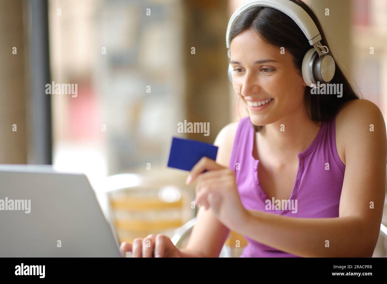 Glückliche Frau, die Kopfhörer trägt und online ppv-Medieninhalte mit einem Laptop und einer Kreditkarte in einem Café kauft Stockfoto