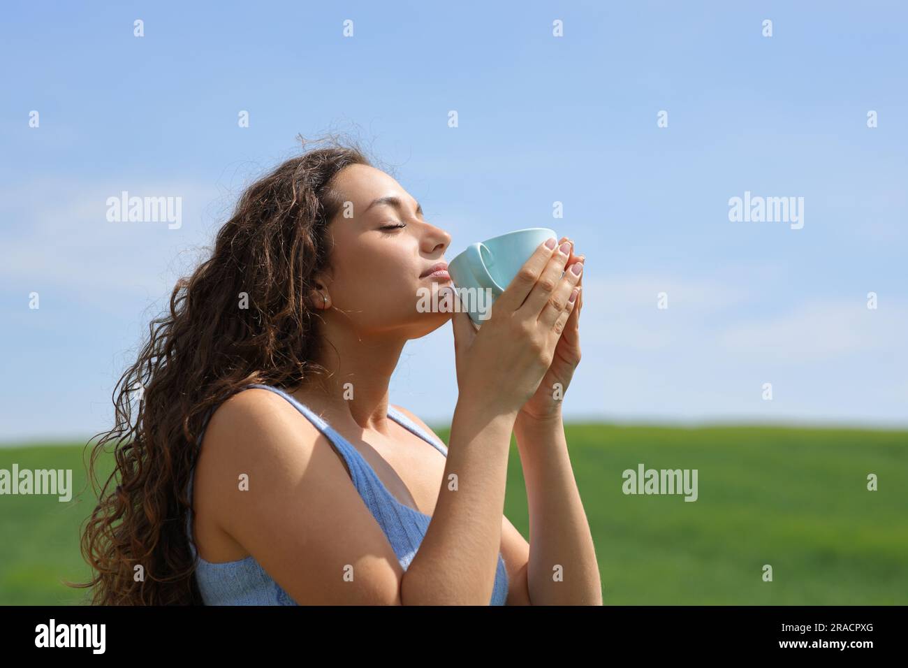 Profil einer Frau, die Kaffee auf einem grünen Feld trinkt Stockfoto