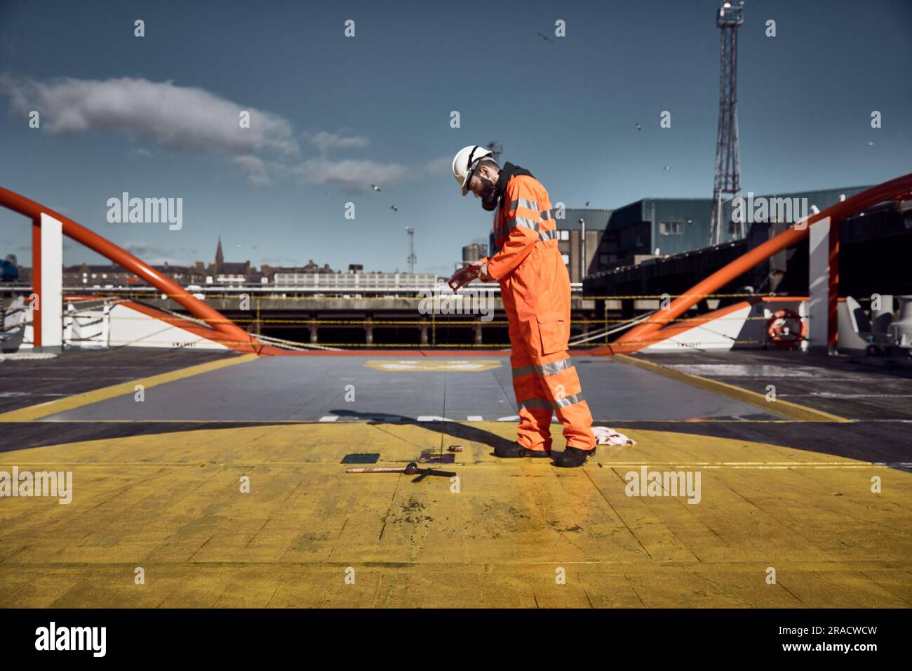 Junger Offshore-Ingenieur, der den Tank für Heizöl auf dem Frachtdeck des Versorgungsschiffs im Hafen manuell abhört. Stockfoto