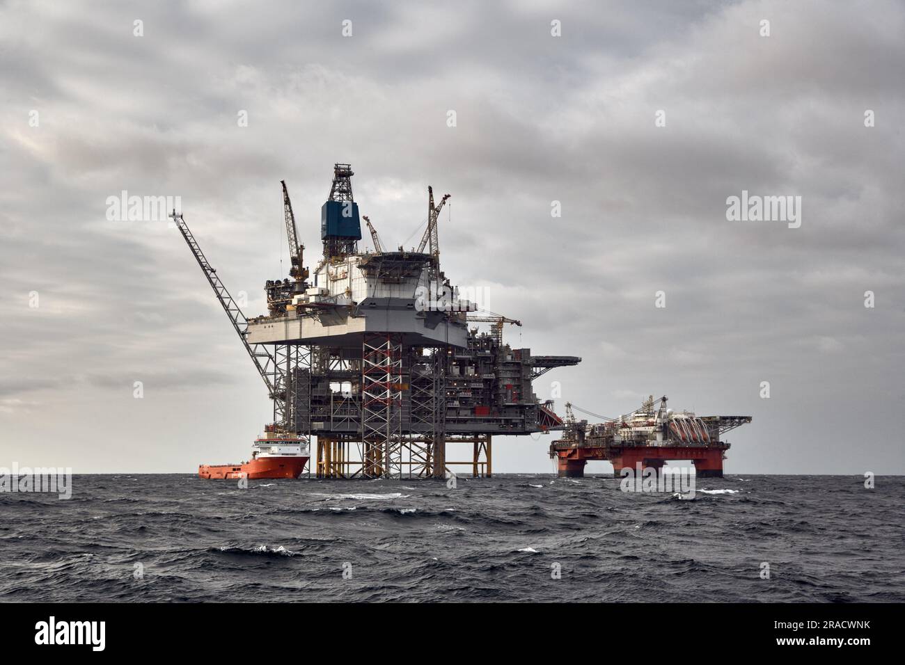 Offshore-Erdöl- und -Erdgasplattform mit Versorgungsschiff, das Frachtaktivitäten durchführt. Dunkler Himmel in der Nordsee. Stockfoto