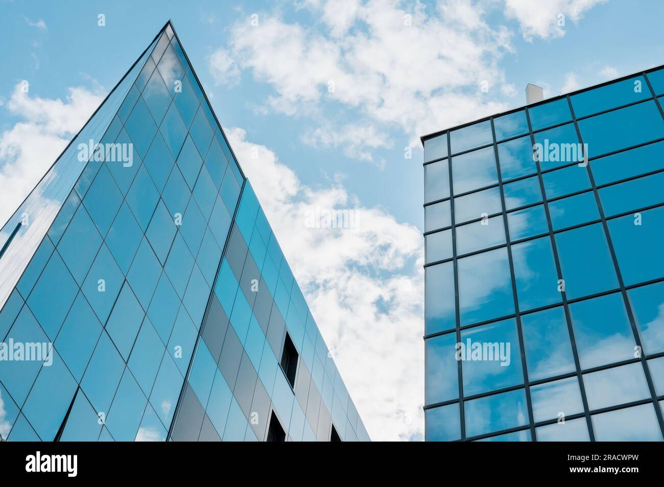 Moderne Fassade aus Glas und Stahl mit Reflexionen. Abstraktes oder grafisches Foto des Himmels mit Wolken, die in ein Gebäude mit Reflektoren hineinragen Stockfoto