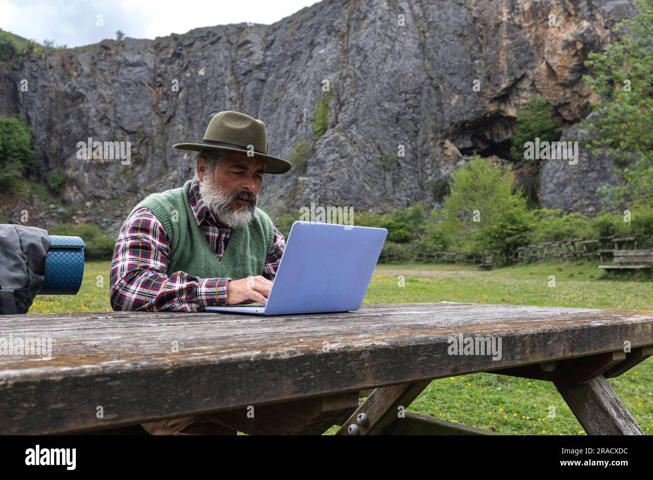 Männlicher Adventurer Backpacker und Hut mit Laptop in einem Tal in den Bergen. Stockfoto