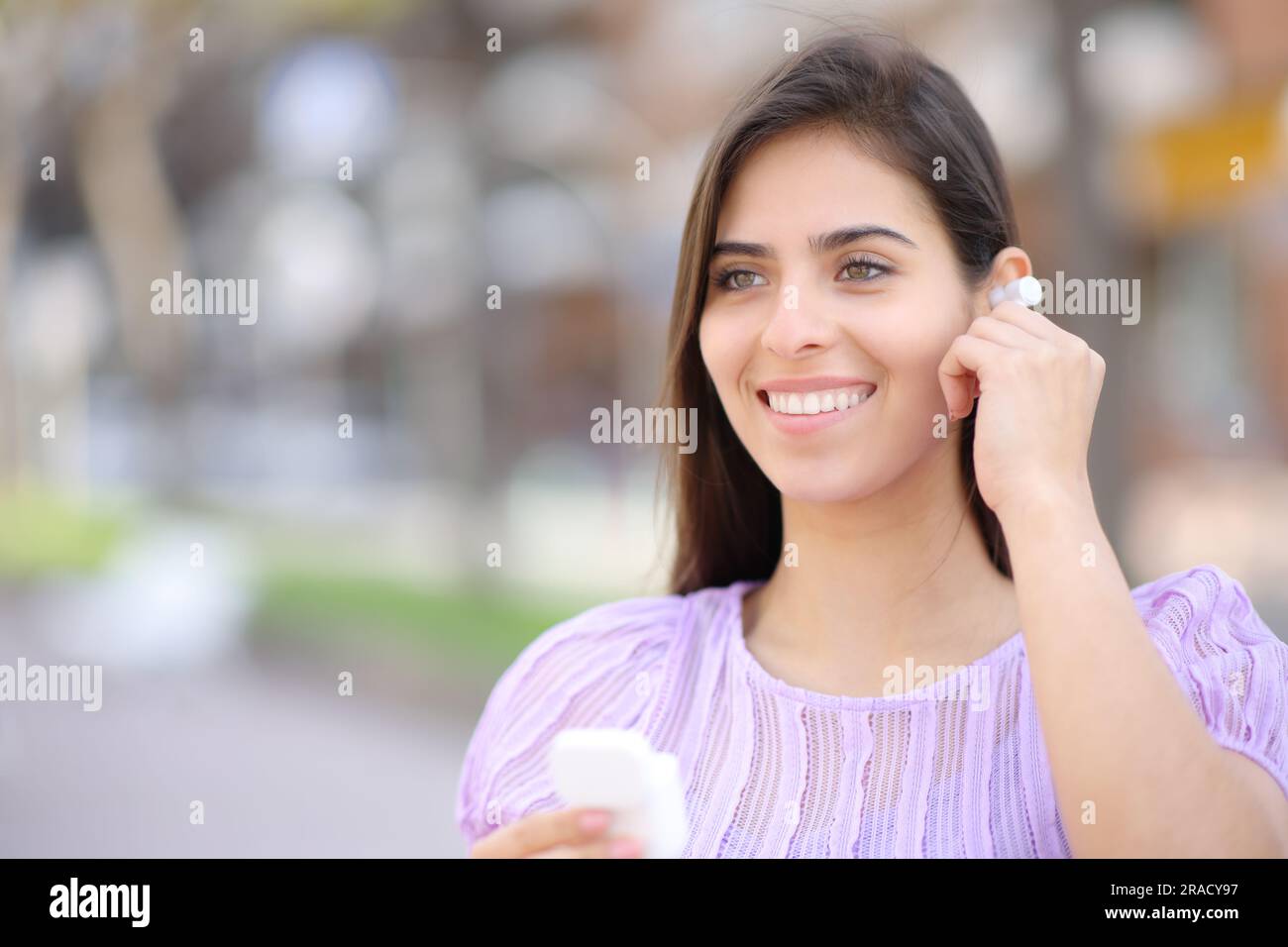 Glückliche Frau, die den Ohrstöpsel auf der Straße aufstellte und wegblickte Stockfoto